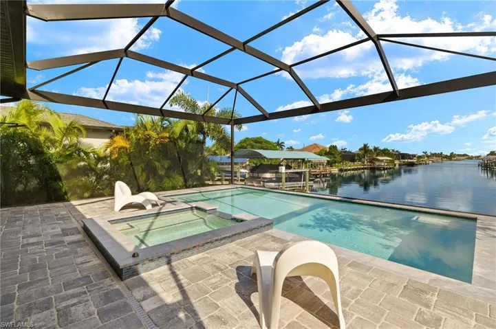 View of pool featuring a lanai, a water view, a patio area, and an in ground hot tub