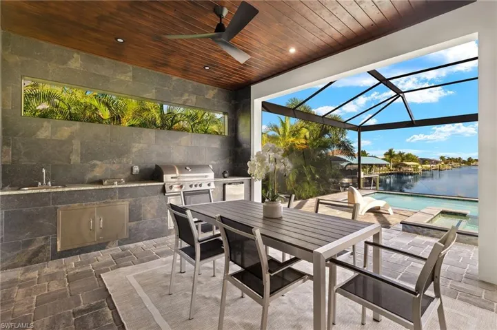 View of patio / terrace with a lanai, a water view, ceiling fan, an outdoor kitchen, and area for grilling