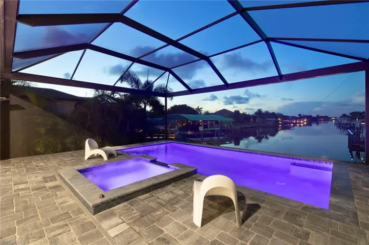 Pool at dusk with glass enclosure, a water view, and a patio area
