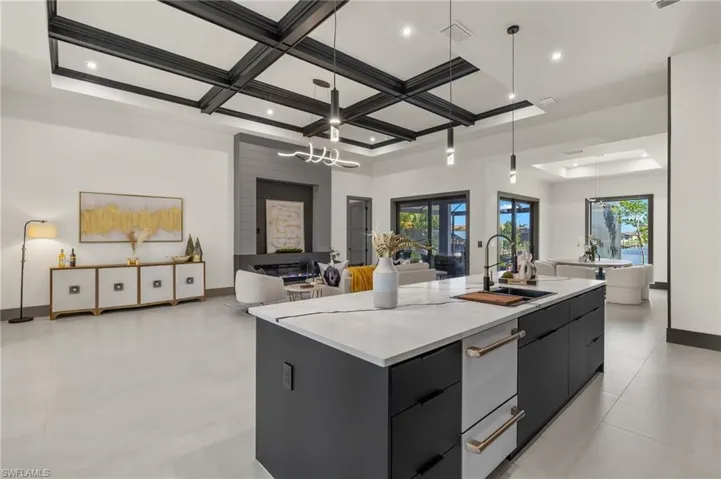 Kitchen with a kitchen island with sink, coffered ceiling, sink, and hanging light fixtures