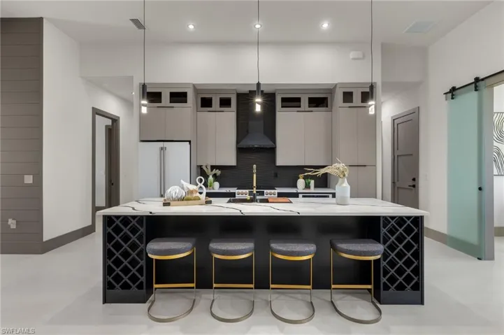 Kitchen with decorative light fixtures, wall chimney exhaust hood, high end white refrigerator, a large island with sink, and a barn door