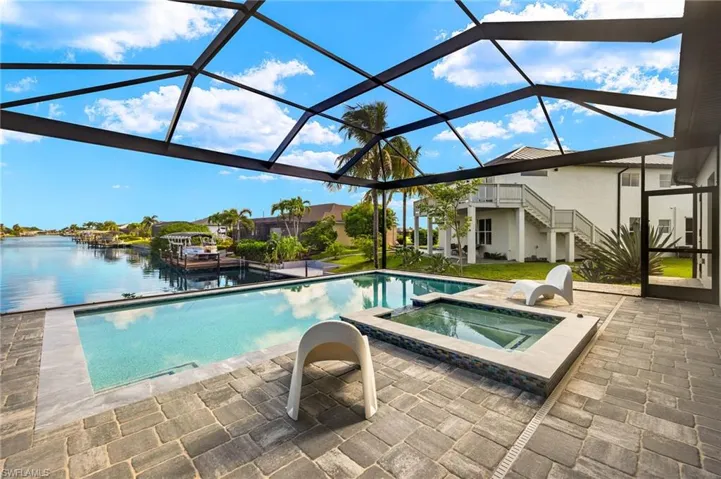 View of swimming pool featuring a water view, a lanai, a patio, and an in ground hot tub
