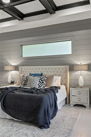Bedroom featuring multiple windows, coffered ceiling, beam ceiling, and wood walls