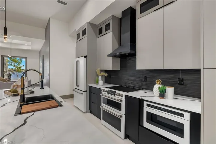 Kitchen with wall chimney exhaust hood, white appliances, pendant lighting, backsplash, and sink