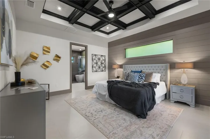 Bedroom with beam ceiling, coffered ceiling, wood walls, ceiling fan, and connected bathroom