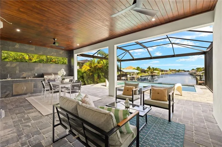 View of patio / terrace with grilling area, a lanai, an outdoor living space, ceiling fan, and a water view