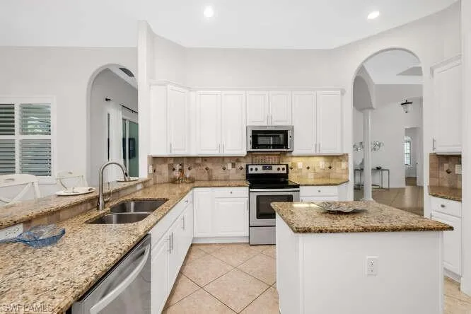 Kitchen with light stone counters, a sink, arched walkways, backsplash, and appliances with stainless steel finishes