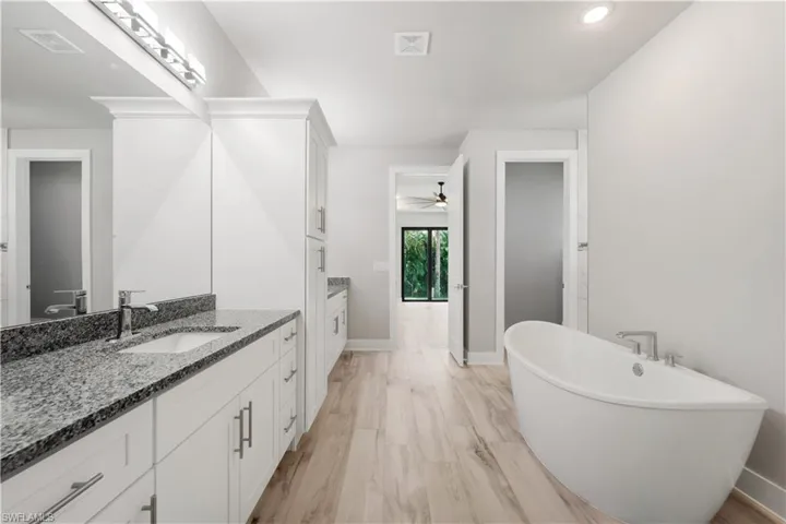 Full bathroom with two vanities, a freestanding tub, visible vents, a sink, and baseboards