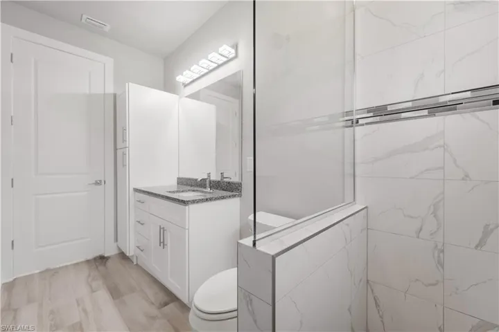 Bathroom featuring visible vents, toilet, vanity, and walk in shower