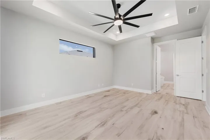 Unfurnished bedroom featuring visible vents, baseboards, a tray ceiling, recessed lighting, and light wood-style flooring