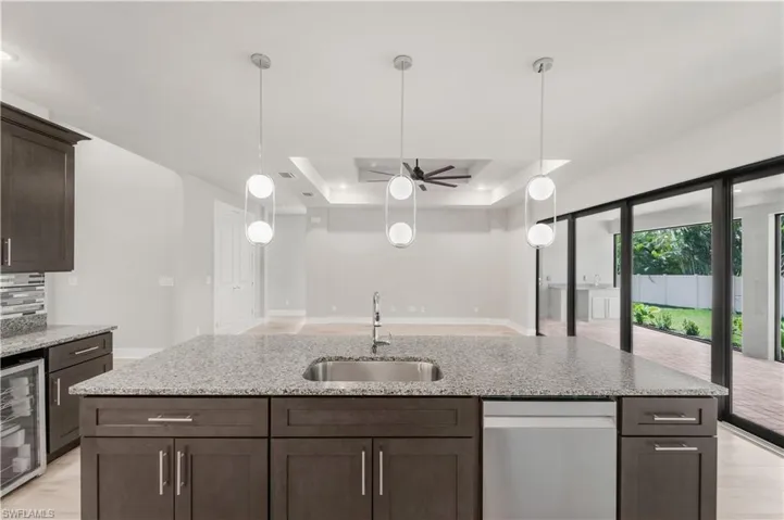 Kitchen with dark brown cabinets, decorative light fixtures, a tray ceiling, beverage cooler, and a sink