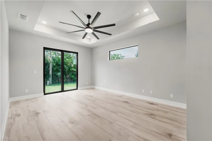 Empty room featuring a tray ceiling, ceiling fan, visible vents, and recessed lighting