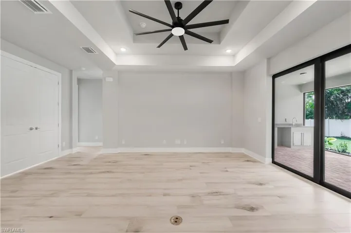 Empty room with a tray ceiling, light wood-type flooring, a ceiling fan, and visible vents