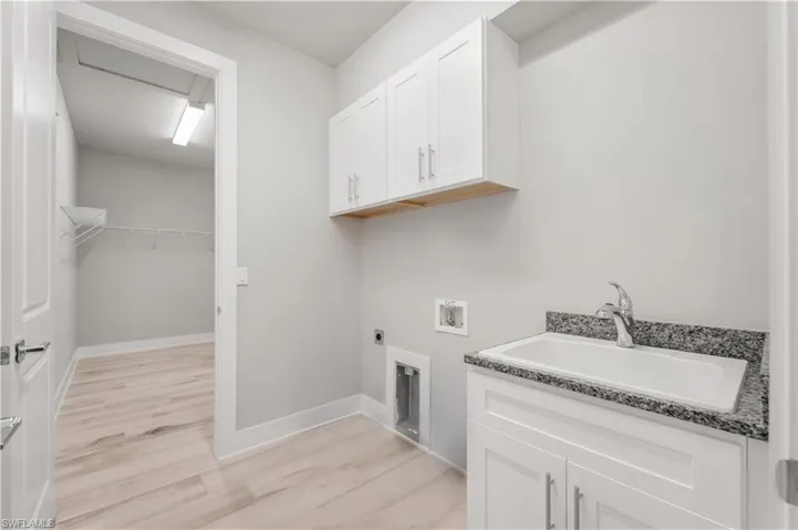 Laundry room with hookup for a washing machine, hookup for an electric dryer, a sink, light wood finished floors, and cabinet space