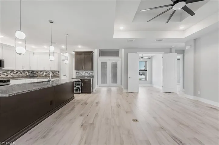 Kitchen with tasteful backsplash, a raised ceiling, a ceiling fan, wine cooler, and a sink