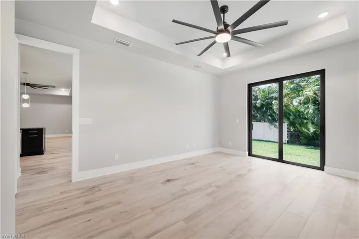 Empty room featuring ceiling fan, a tray ceiling, light wood-type flooring, recessed lighting, and baseboards