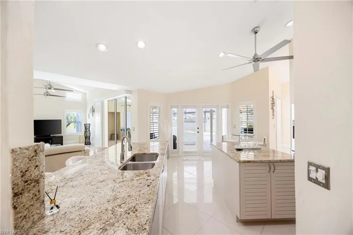 Kitchen with a ceiling fan, lofted ceiling, light stone counters, light tile patterned flooring, and open floor plan
