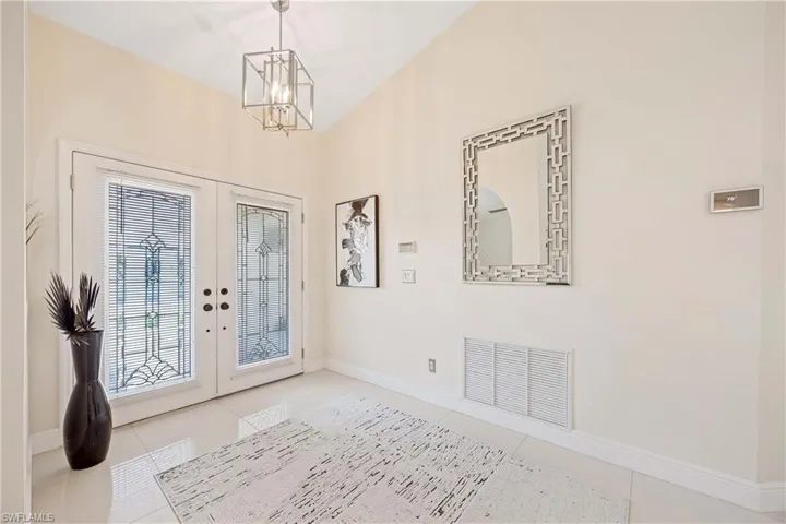 Foyer entrance featuring french doors, a chandelier, and light tile