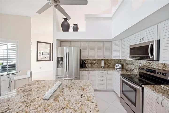 Kitchen featuring stainless steel appliances, light stone countertops, light tile patterned floors, a ceiling fan, and white cabinetry