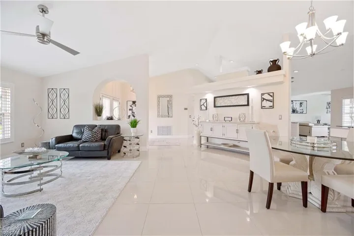 Living room with lofted ceiling, a chandelier, arched walkways, a ceiling fan, and light tile