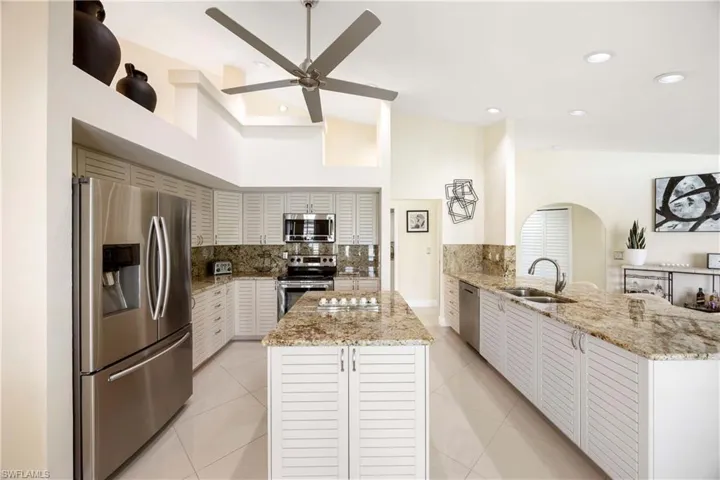 Kitchen with appliances with stainless steel finishes, light stone countertops, backsplash, arched walkways, and a peninsula