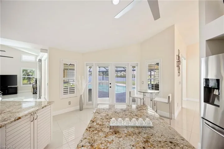 Kitchen featuring lofted ceiling, stainless steel fridge, light stone counters, ceiling fan, and light tile patterned floors