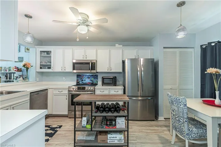 Kitchen with hanging light fixtures, stainless steel appliances, light countertops, and glass insert cabinets