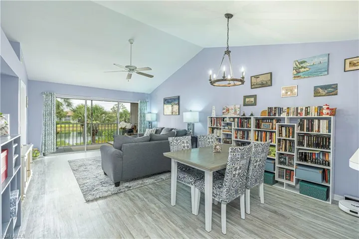 Dining area featuring a water view, light wood-type flooring, a chandelier, high vaulted ceiling, and a ceiling fan