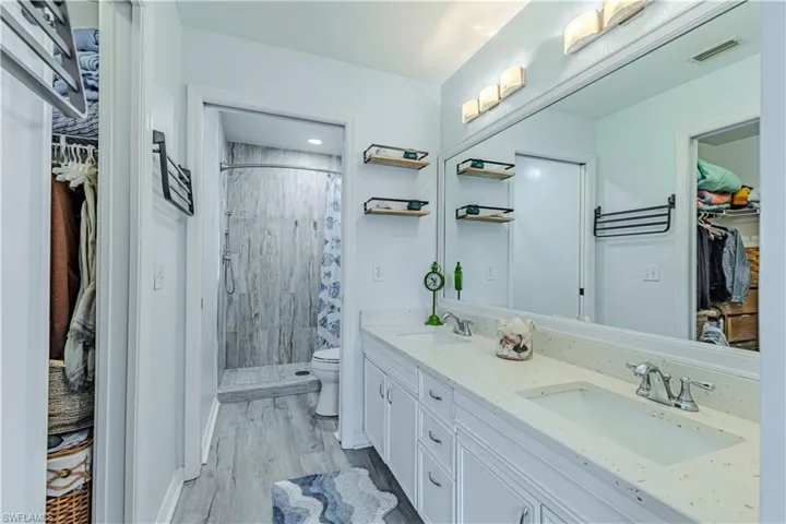 Bathroom featuring a spacious closet, a shower stall, double vanity, and light wood-style flooring