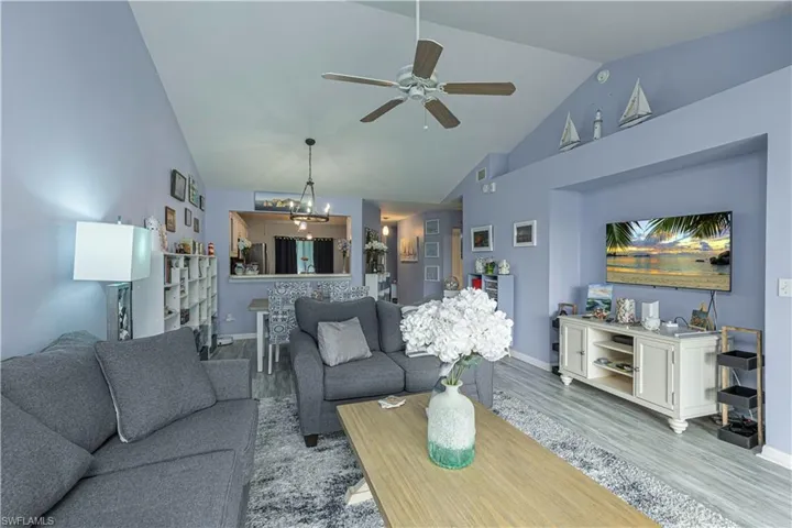 Living area featuring wood finished floors, vaulted ceiling, a chandelier, and ceiling fan