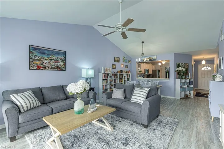 Living area with light wood-style floors, ceiling fan, high vaulted ceiling, and a chandelier