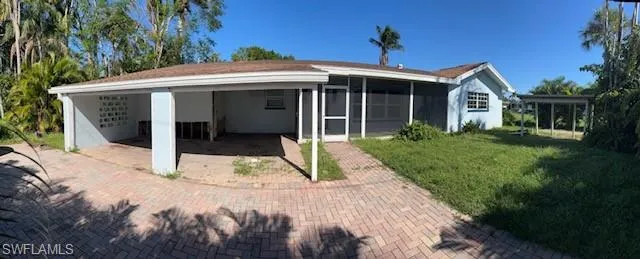 Rear view of house featuring a sunroom, a carport, and a lawn