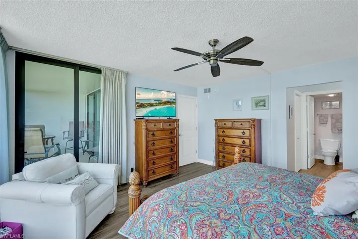 Bedroom with dark wood-style floors, access to exterior, a ceiling fan, and a textured ceiling