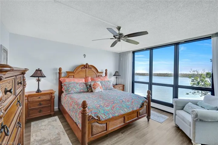 Bedroom with expansive windows, a water view, a textured ceiling, and wood finished floors