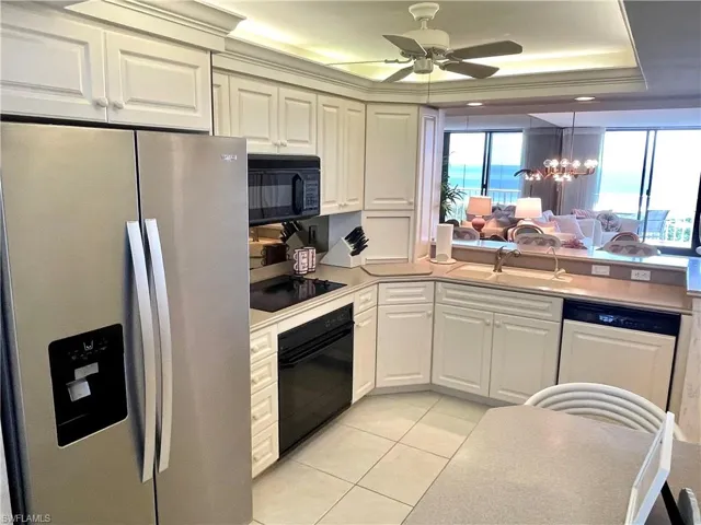 Kitchen with pendant lighting, sink, white cabinetry, black appliances, and a raised ceiling