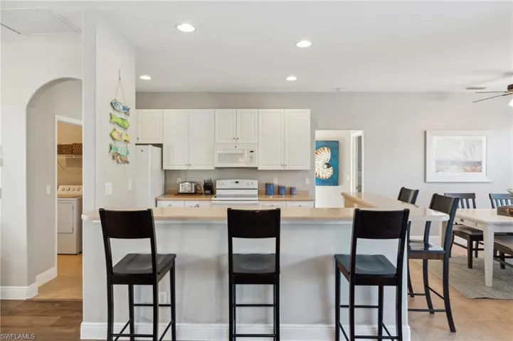 Kitchen with a kitchen breakfast bar, white appliances, white cabinets with a breakfast nook to the right.