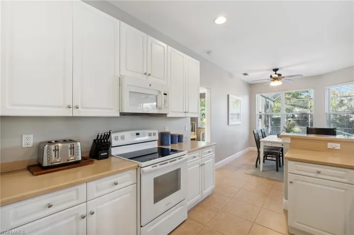 Kitchen featuring light tile patterned floors, white appliances, white cabinetry, and ceiling fan in dining nook.