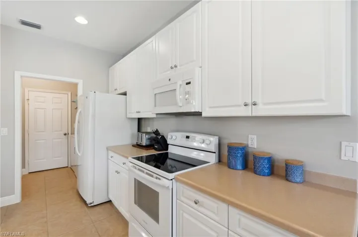 Kitchen with light tile patterned floors, white cabinets, and white appliances. Laundry is off the kitchen leading to garage.