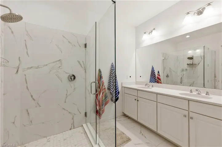 Bathroom featuring double vanity, a marble finish shower, and light marble finish flooring