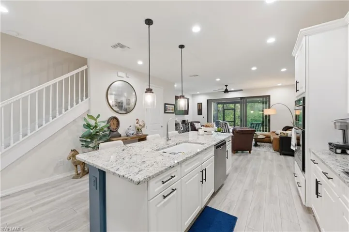 Kitchen with white cabinets, light stone countertops, open floor plan, light wood finished floors, and a ceiling fan