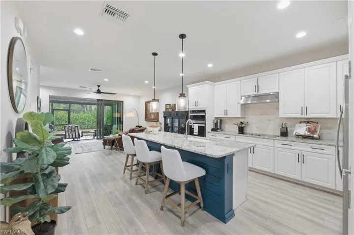 Kitchen featuring white cabinetry, open floor plan, light stone countertops, hanging light fixtures, and a kitchen island with sink