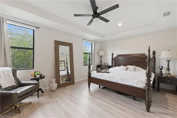Bedroom with a raised ceiling, light wood-type flooring, a ceiling fan, and recessed lighting
