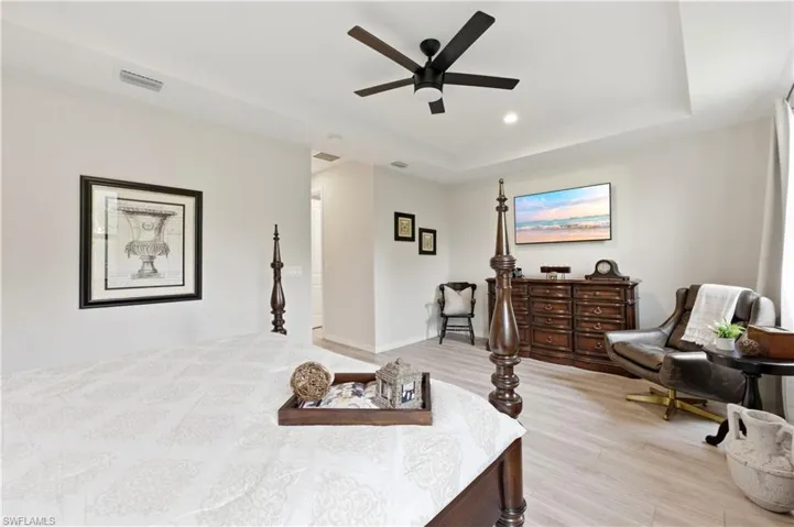 Bedroom with light wood finished floors, a tray ceiling, a ceiling fan, and recessed lighting