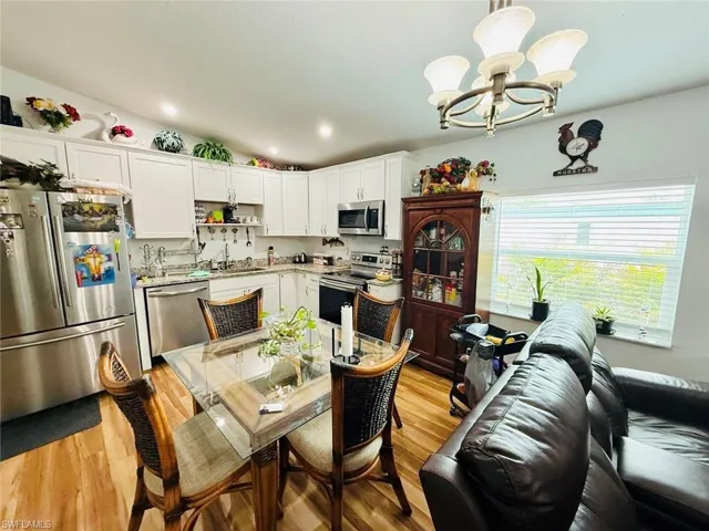 Kitchen with vaulted ceiling, stainless steel appliances, a chandelier, light wood finished floors, and white cabinetry