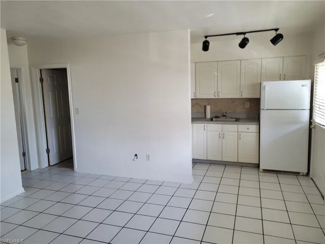 Kitchen featuring light tile patterned floors, white refrigerator, track lighting, sink, and white cabinetry