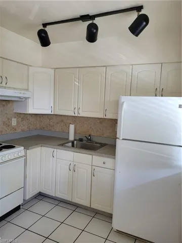 Kitchen featuring light tile patterned floors, ventilation hood, sink, refrigerator, and range