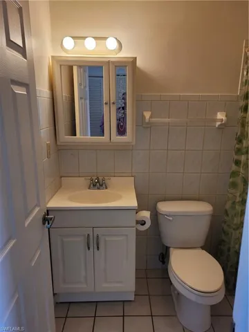 Bathroom with decorative backsplash, tile walls, toilet, tile patterned floors, and vanity