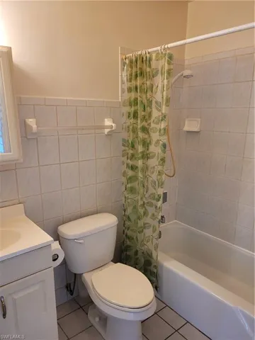 Full bathroom with toilet, tile walls, shower / tub combo with curtain, tile patterned flooring, and vanity