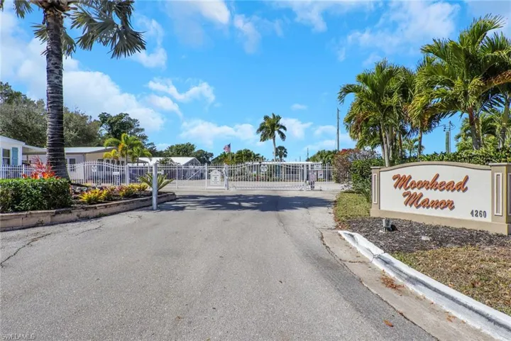 View of asphalt street with a gated entry, a gate, and curbs
