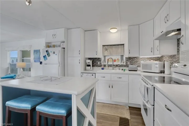 Kitchen featuring white appliances, white cabinetry, a breakfast bar, light countertops, and light wood-style flooring